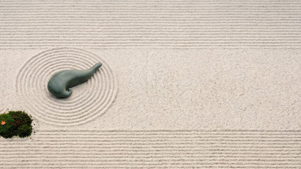 A smooth green stone shaped like a pancreas, lying in raked gravel circles in a Japanese zen garden, beside a cushion of moss